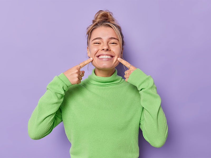 Ragazza bionda sorride indicando i denti